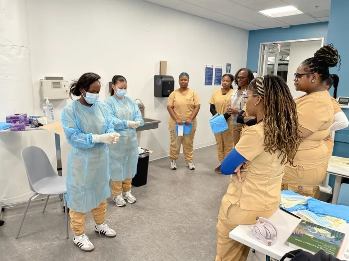 Apprentices in scrubs and gowns working through a practical exercise in a nursing skills lab.