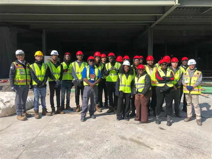A cohort of youth apprentices in high-visibility vests and hard hats, gathered together on a construction site.