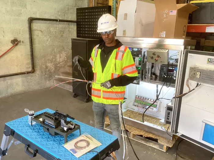 An apprentice in a hard hat and high-visibility vest running fibre at a training station.