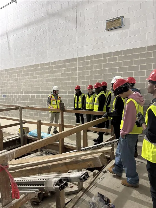 Apprentices in high-visibility vests inspecting timber formwork on a site visit.