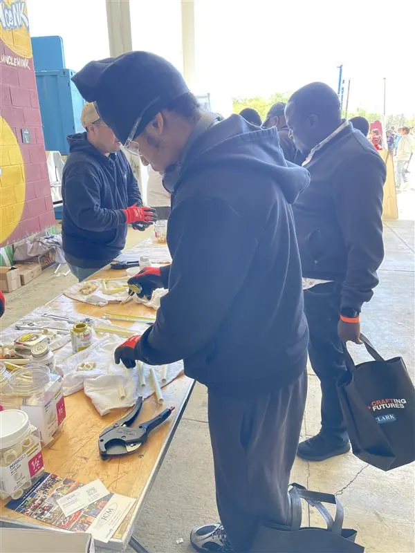 Apprentices trying hand tools at an outdoor workbench.