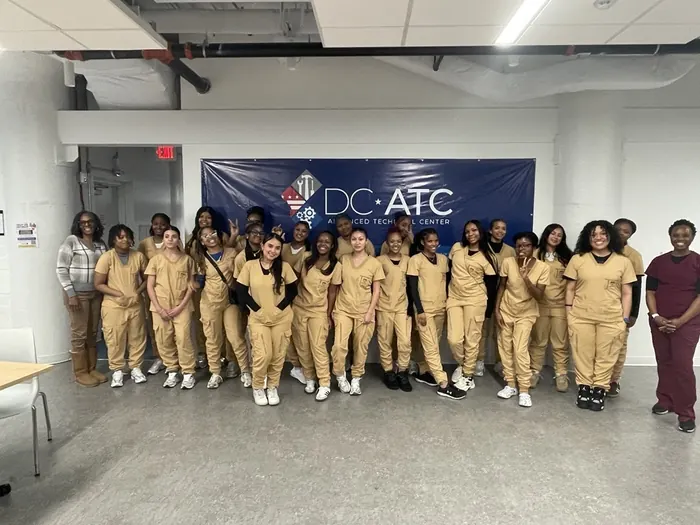 A cohort of health apprentices in scrubs standing together in front of a DC Advanced Technical Center banner.